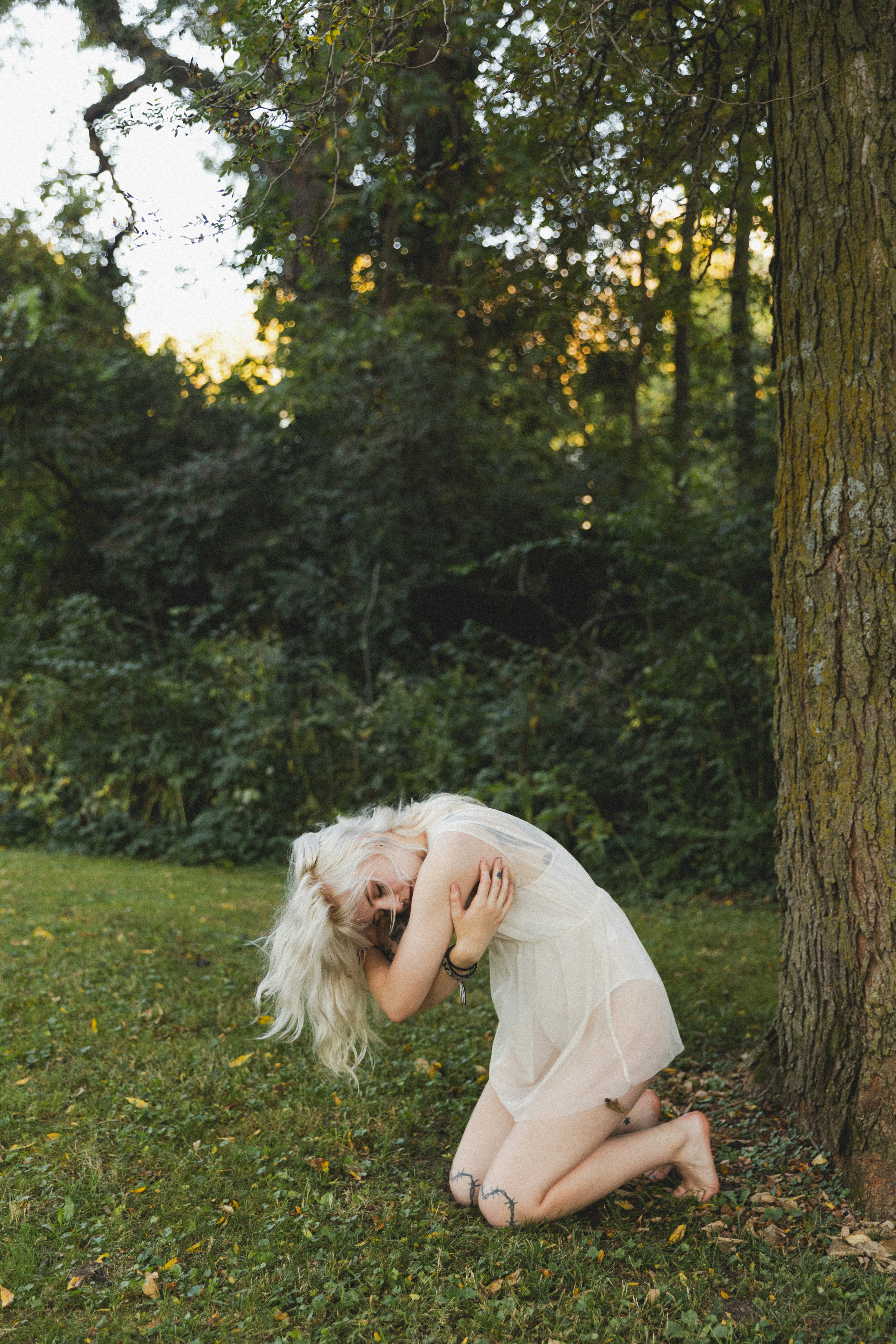 A woman kneeling in the grass next to a tree