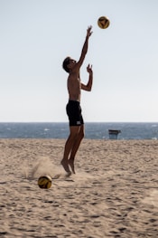 A man jumping up to catch a ball on the beach