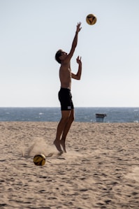 A man jumping up to catch a ball on the beach