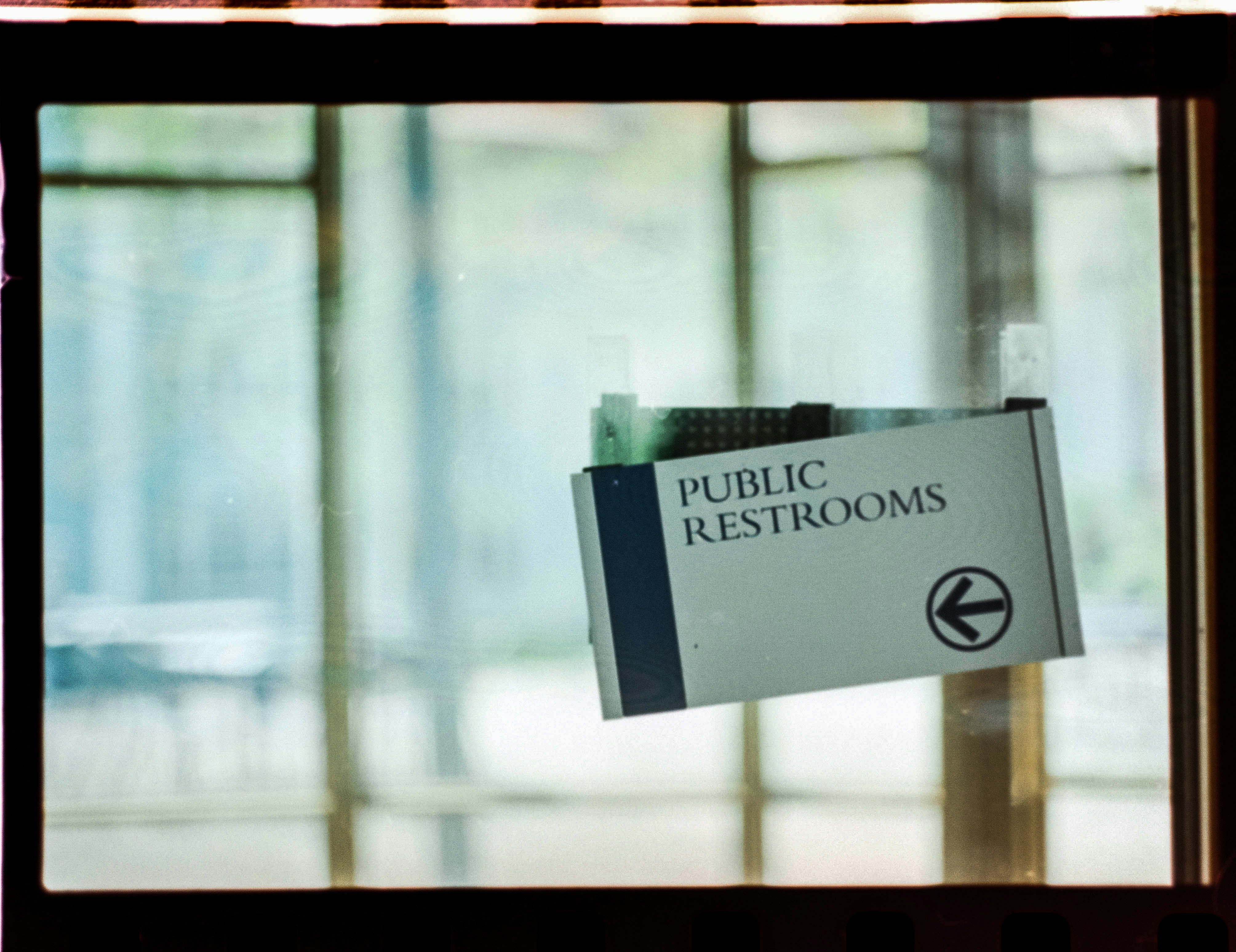 A public restroom sign hanging from the side of a window