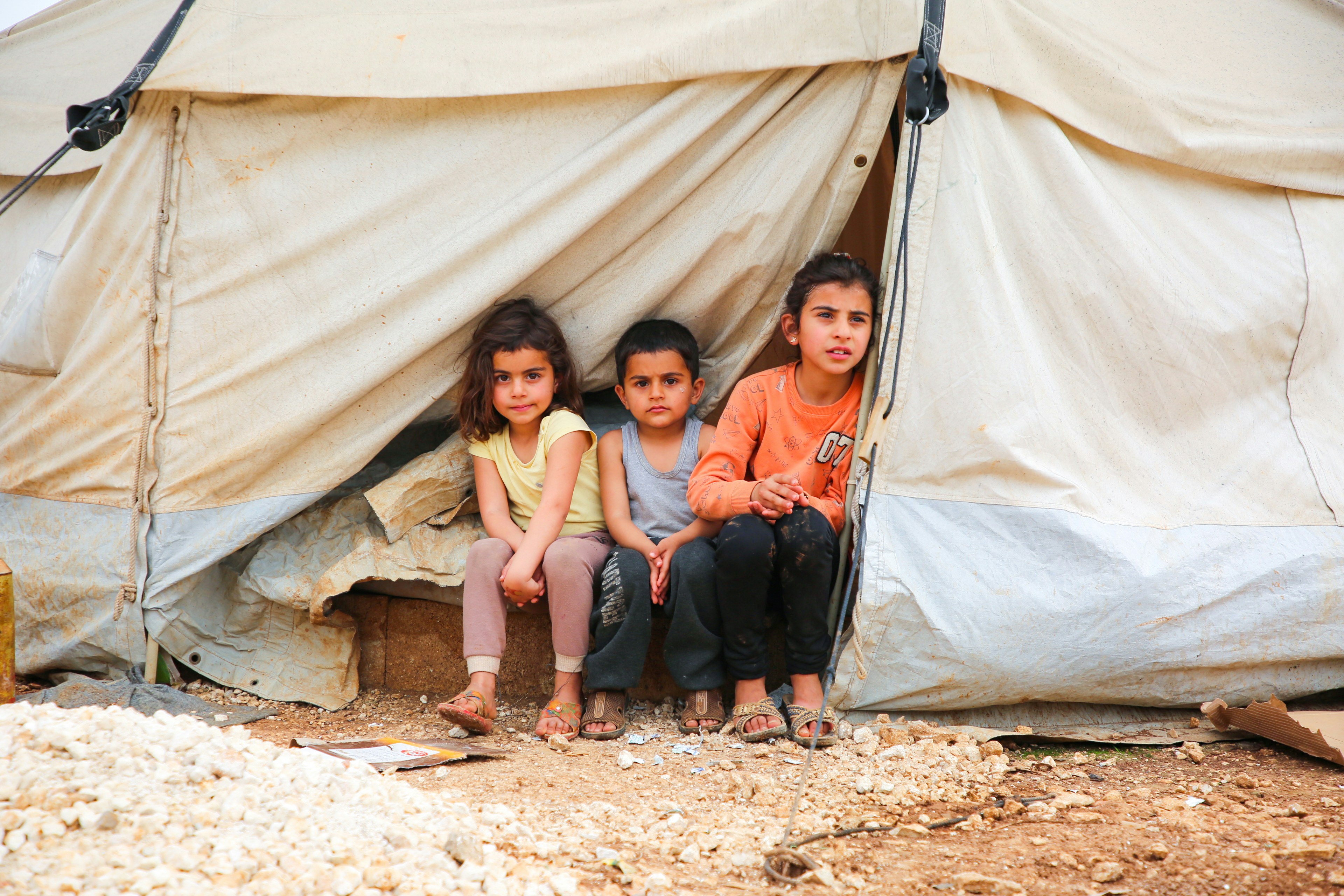 Three children sitting in front of a tent