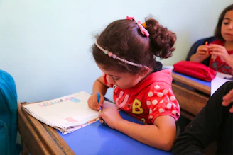 A little girl sitting at a desk writing on a piece of paper