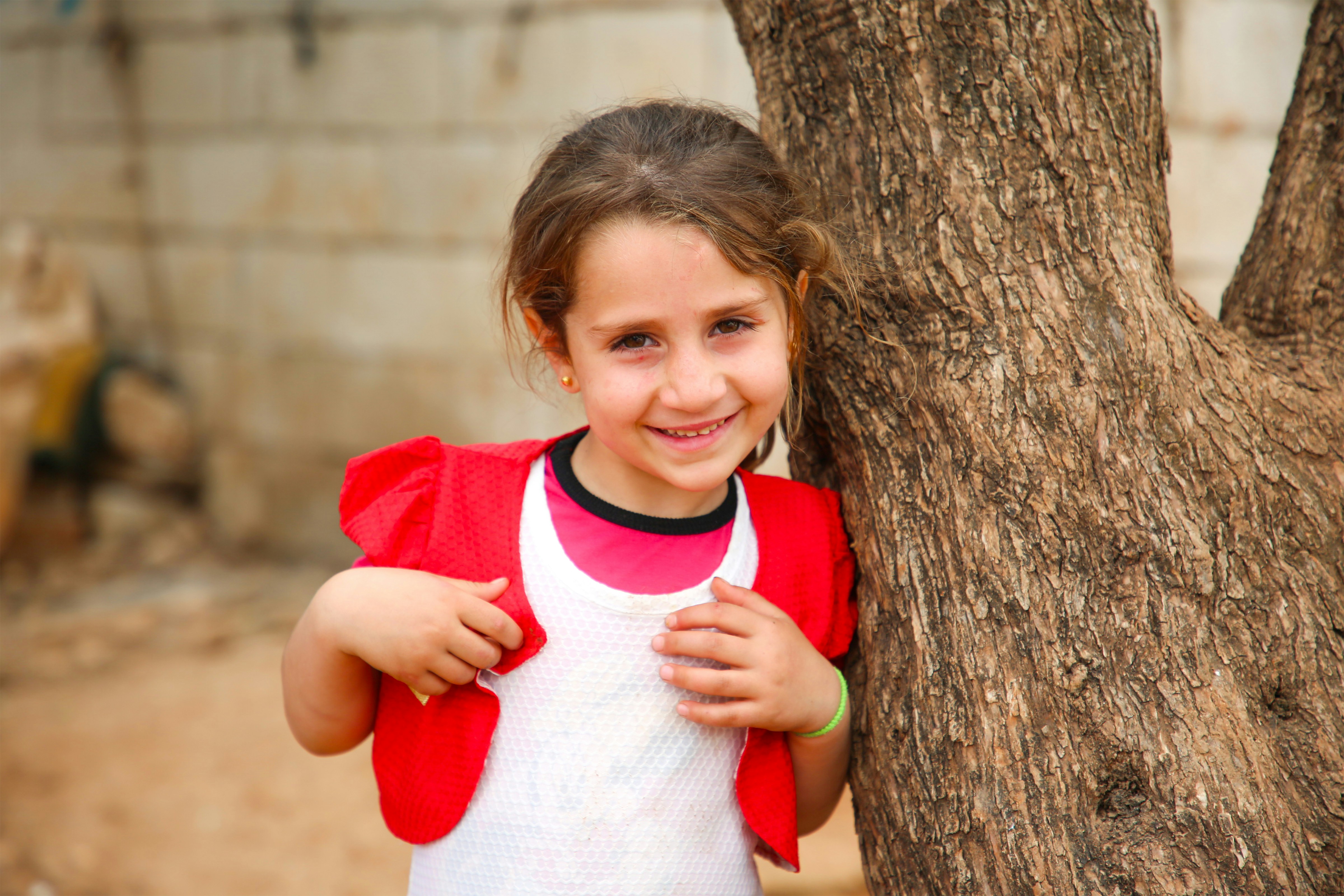 A little girl standing next to a tree