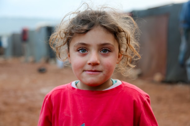 A little girl in a red shirt standing in a dirt field