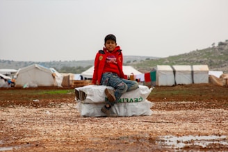 A young boy sitting on top of a bag in the mud
