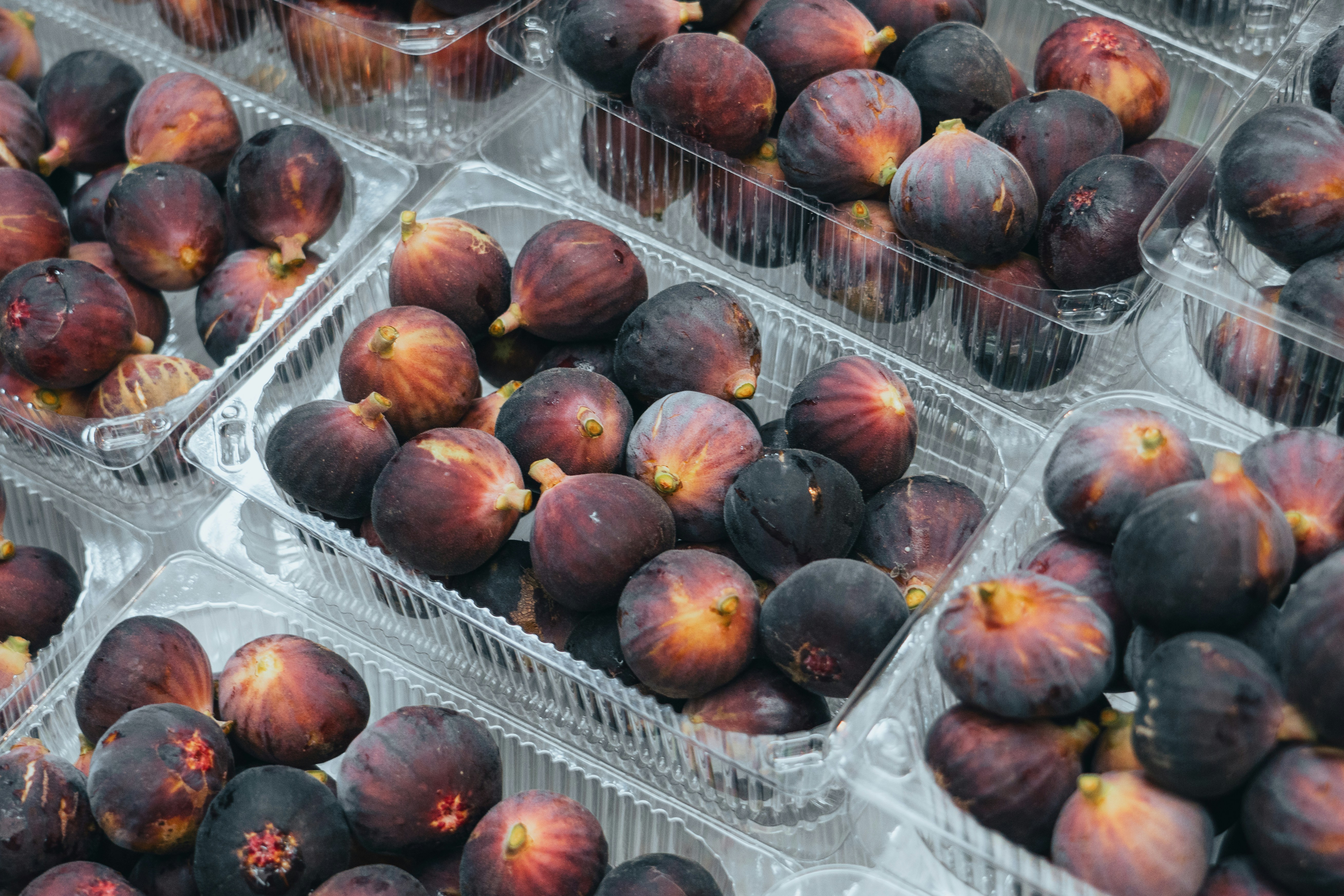 A bunch of plastic containers filled with lots of plums