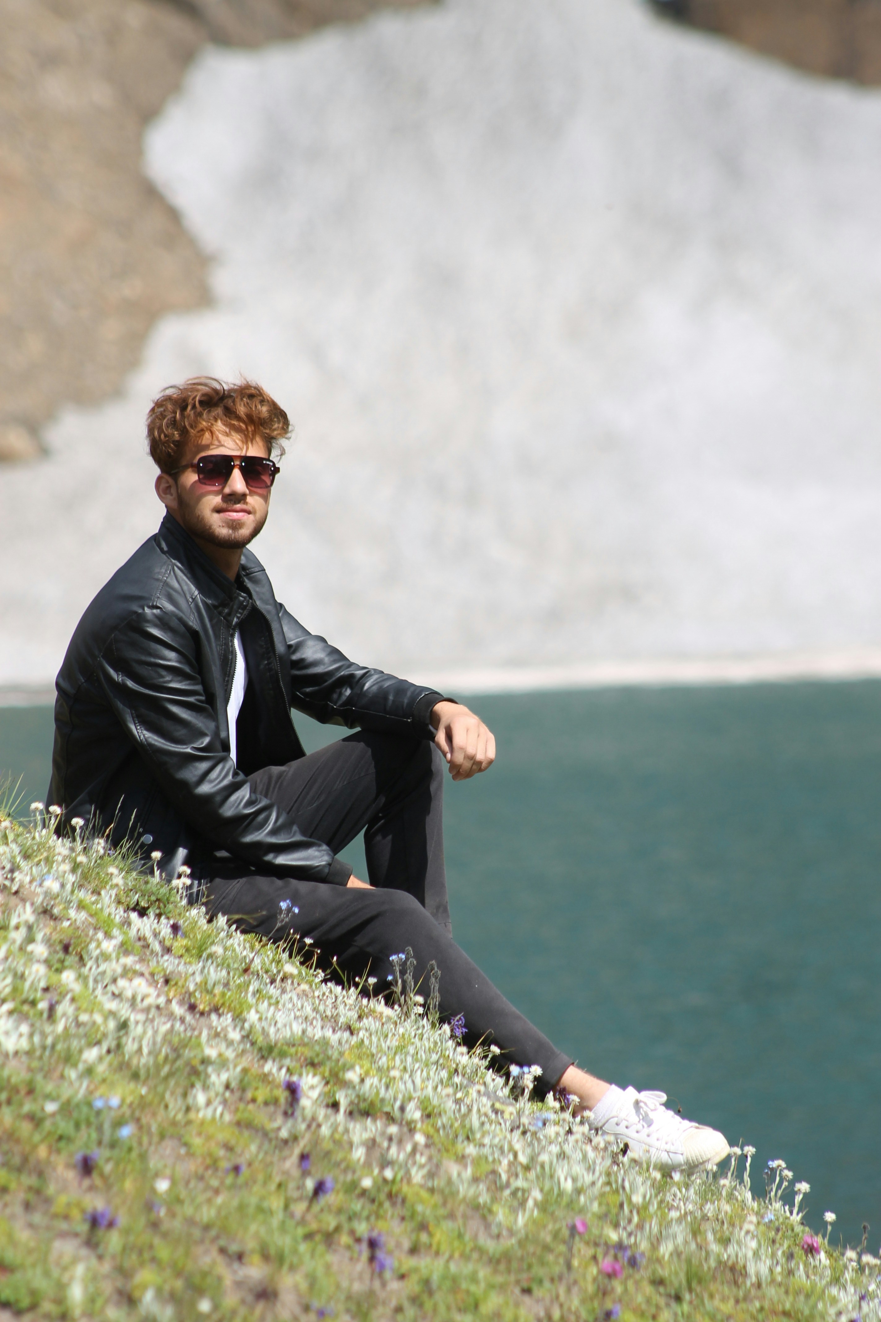 A man sitting on top of a hill next to a lake
