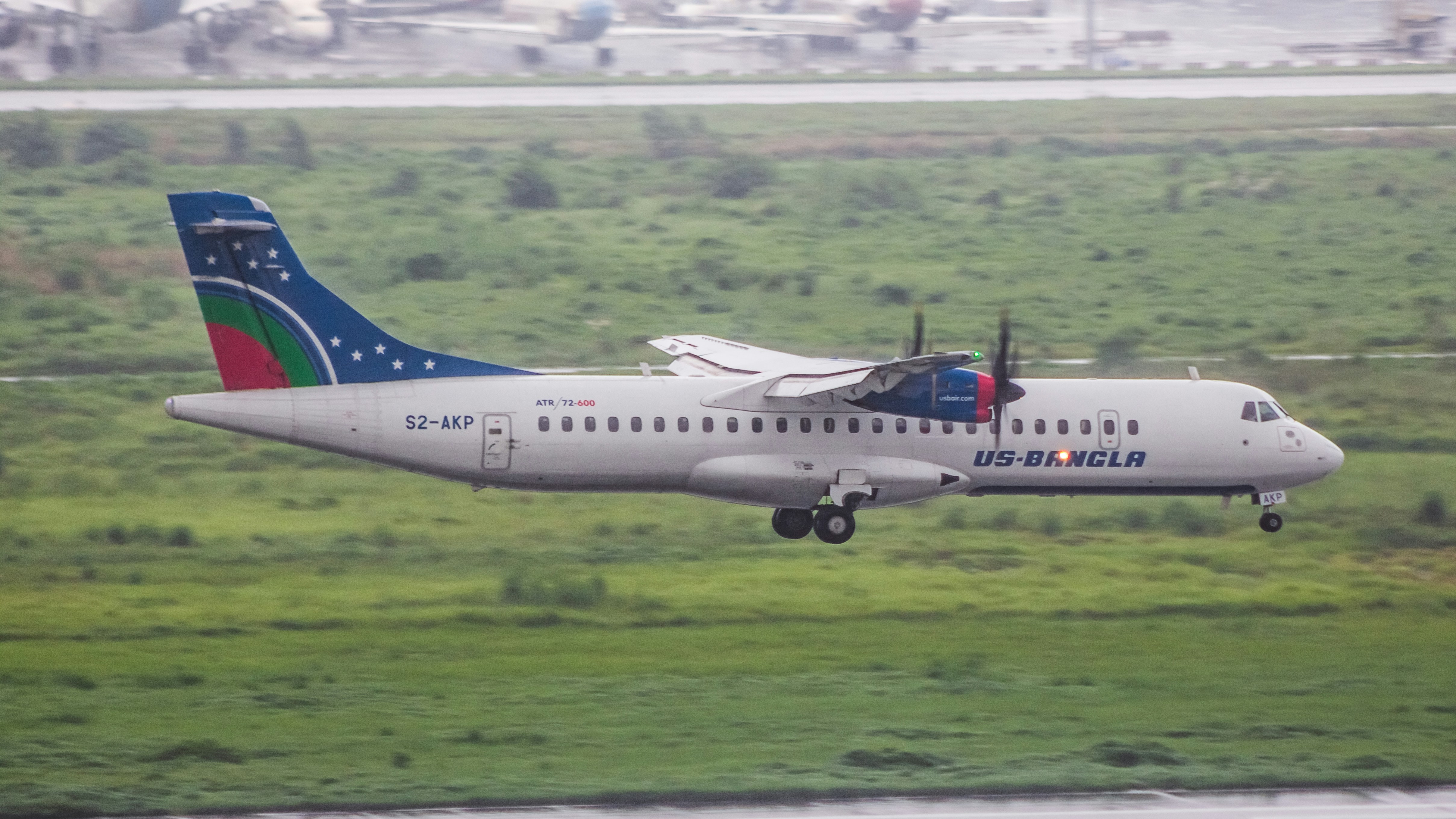 A large passenger jet flying over a lush green field, 