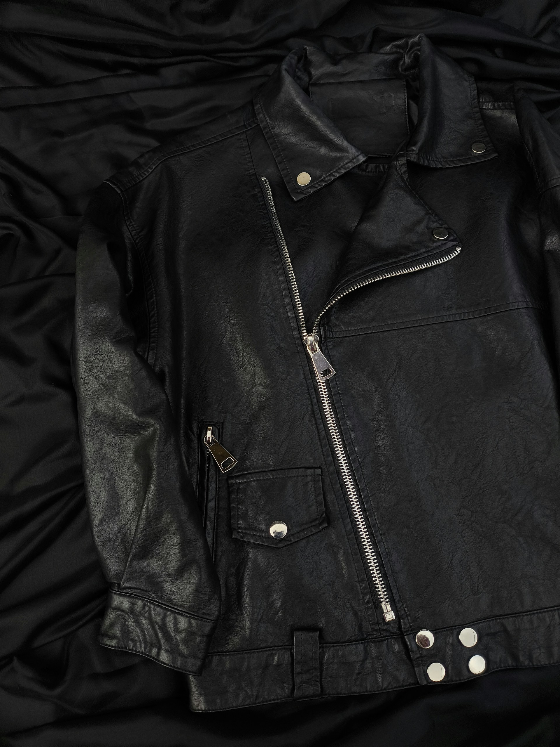 A black leather jacket laying on a black cloth