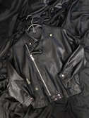 A black leather jacket laying on top of a bed