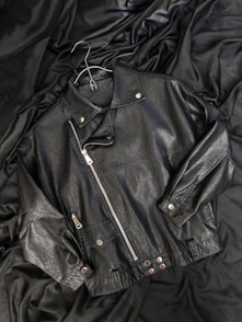 A black leather jacket laying on top of a bed