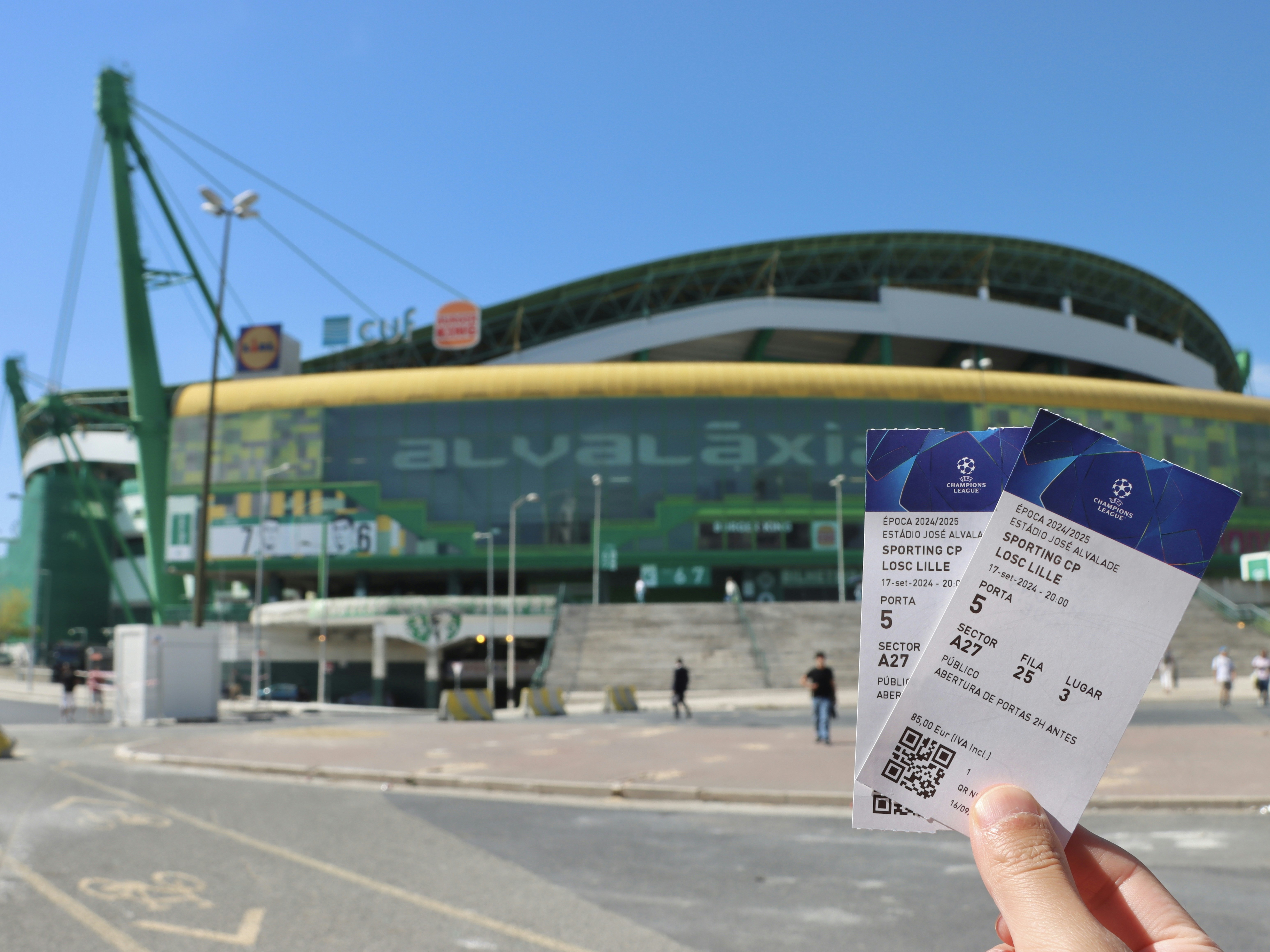 A person holding up two tickets in front of a stadium
