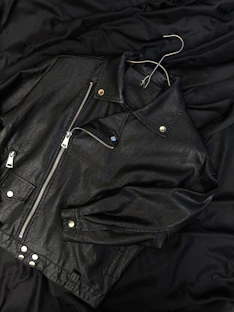 A black leather jacket laying on top of a bed