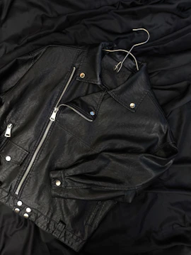 A black leather jacket laying on top of a bed