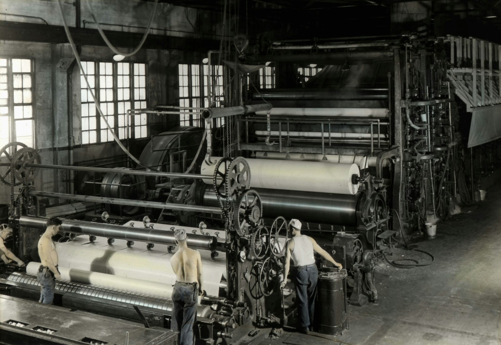 Mill workers operating large industrial machinery on a hot production floor.