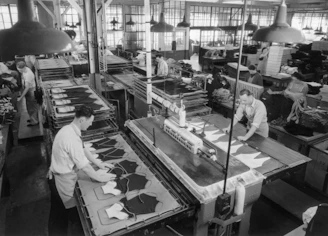 Workers operating machinery in a busy garment factory setting.