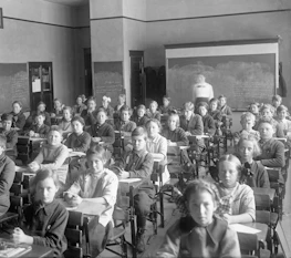 Children sit in a classroom at wooden desks.