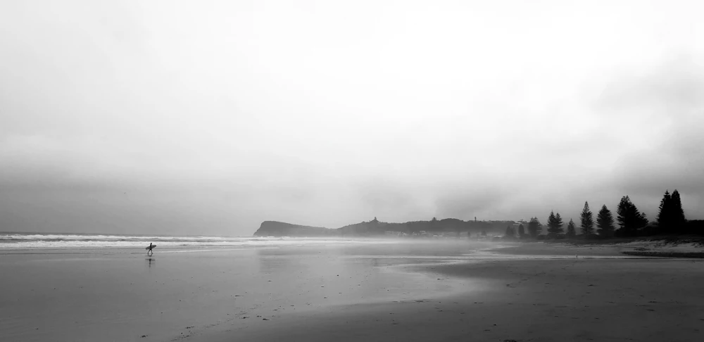 A black and white photograph of an empty beach, evoking Camp Drewe's long history