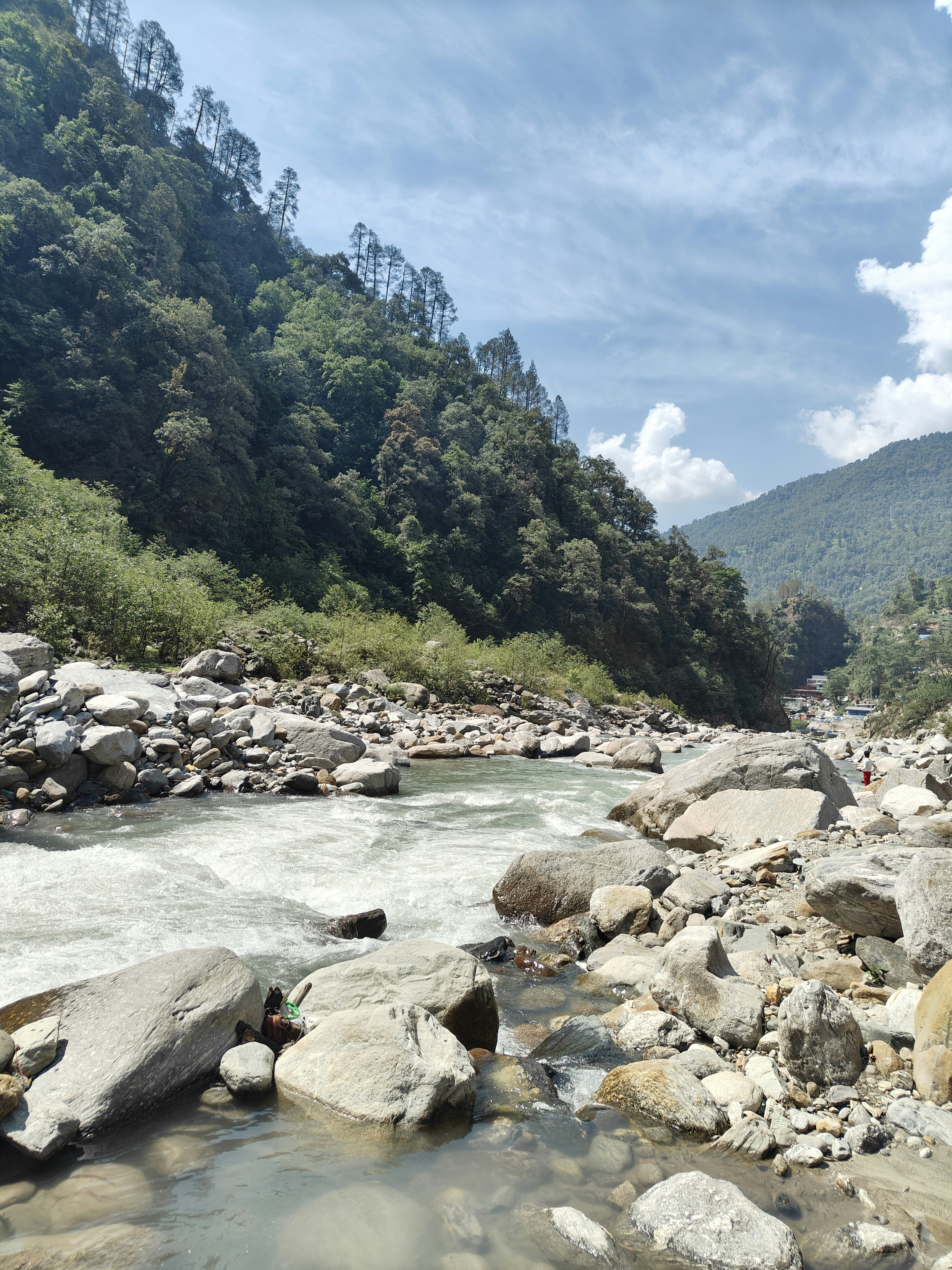 Rishikesh river valley with lush green hills, Ganges river flowing through rocky terrain, bright blue sky, adventure destination