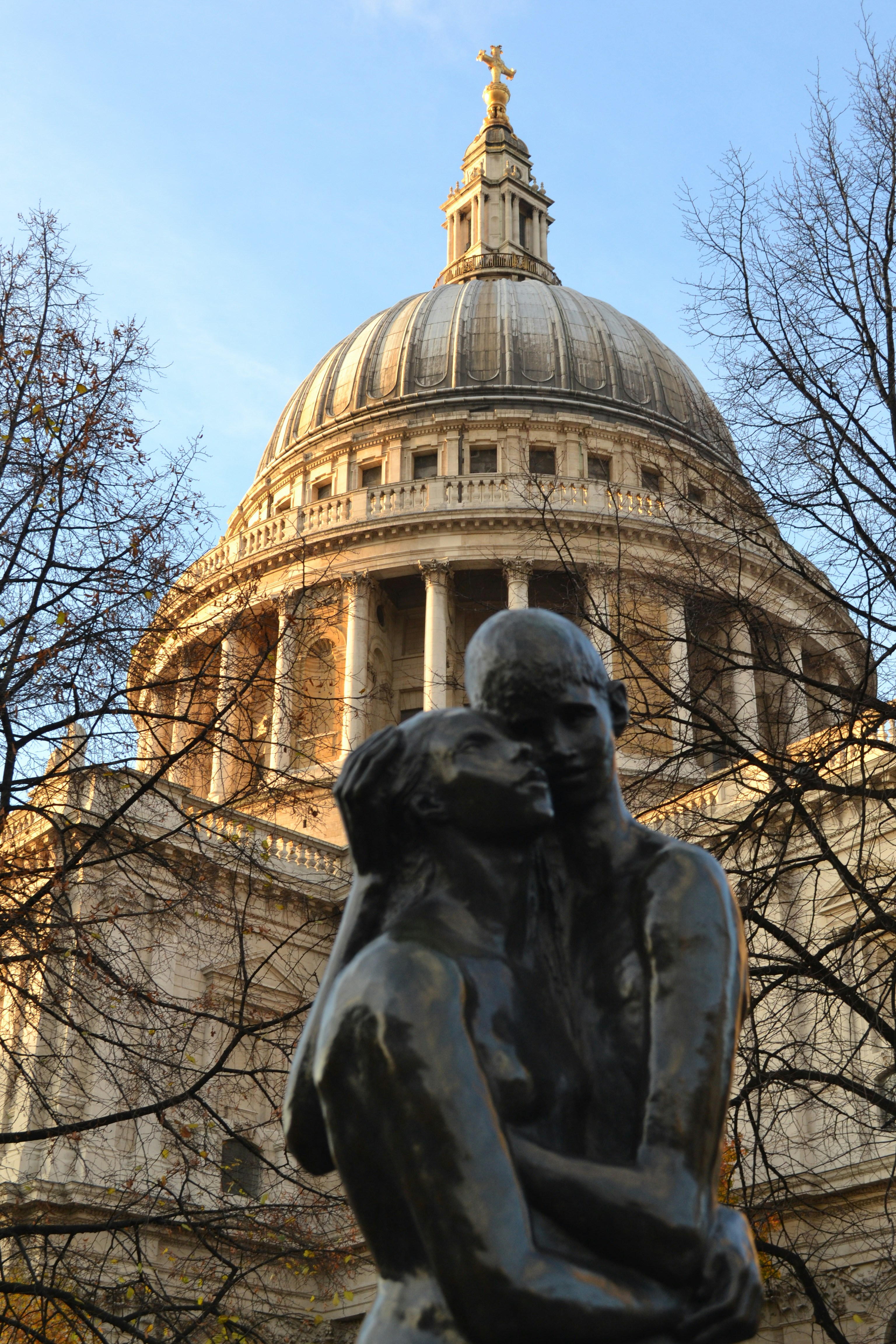 A statue of a man holding a woman in front of a domed building