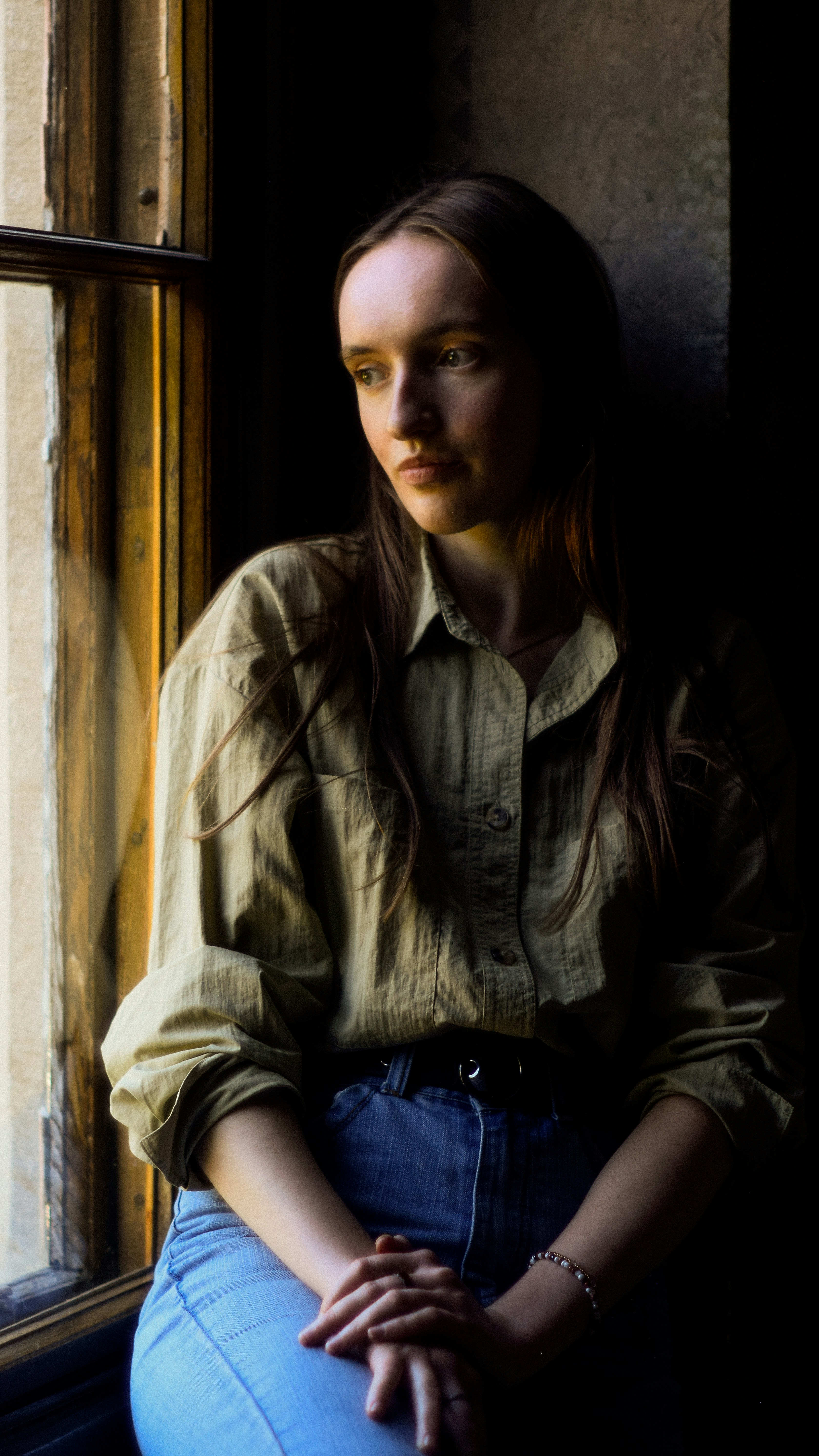 A woman sitting on a window sill looking out the window photo – Free ...