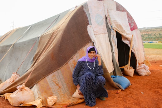 A woman sitting in front of a tent on top of a dirt field