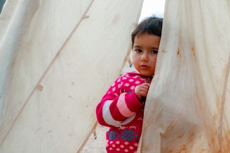 A little girl peeking out from behind a curtain