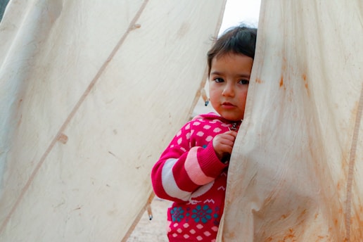 A little girl peeking out from behind a curtain