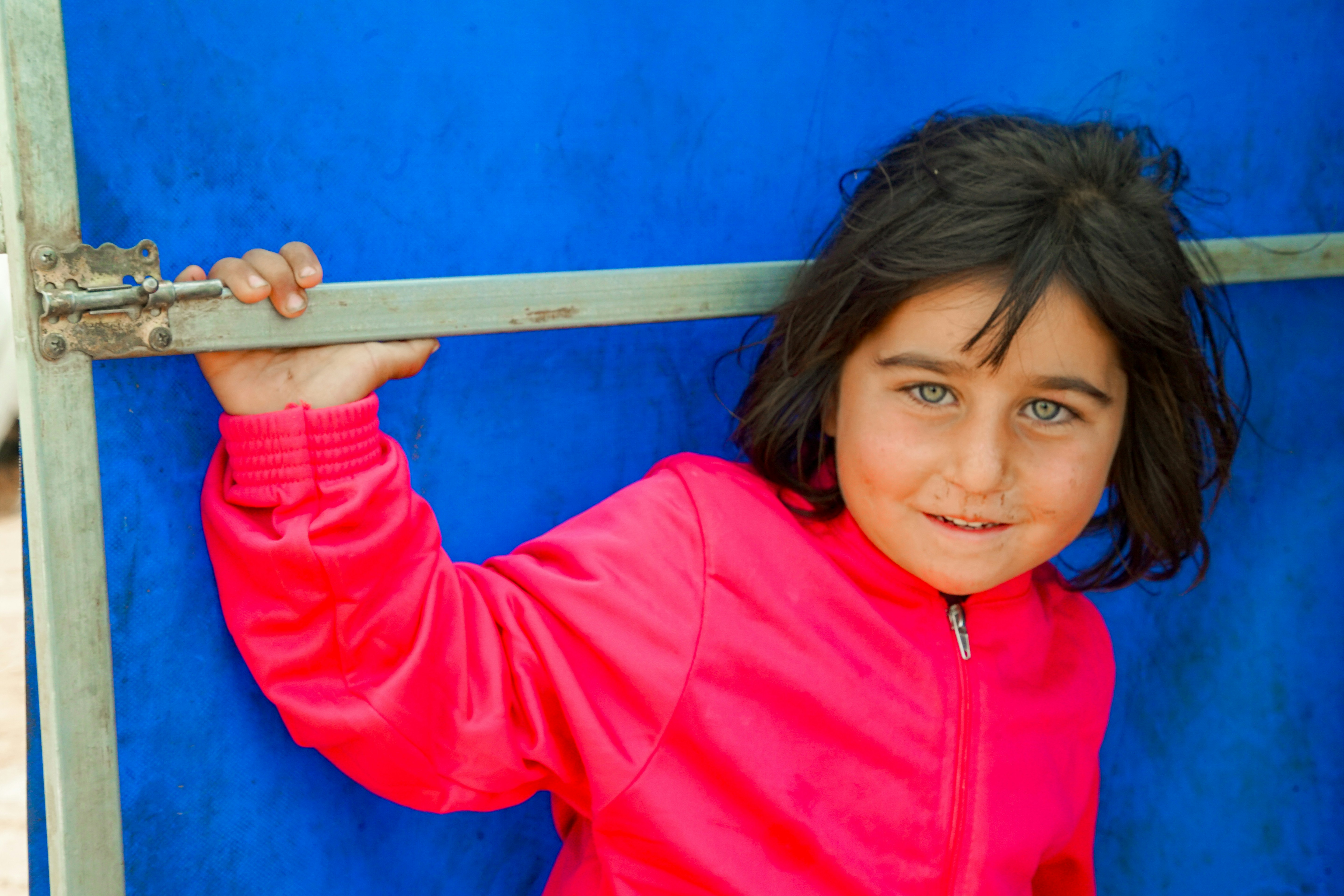 A young girl in a pink jacket holding onto a blue wall