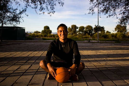 A man sitting on a wooden floor holding a basketball