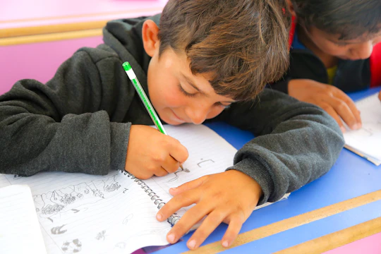 Two young boys sitting at a desk writing on paper