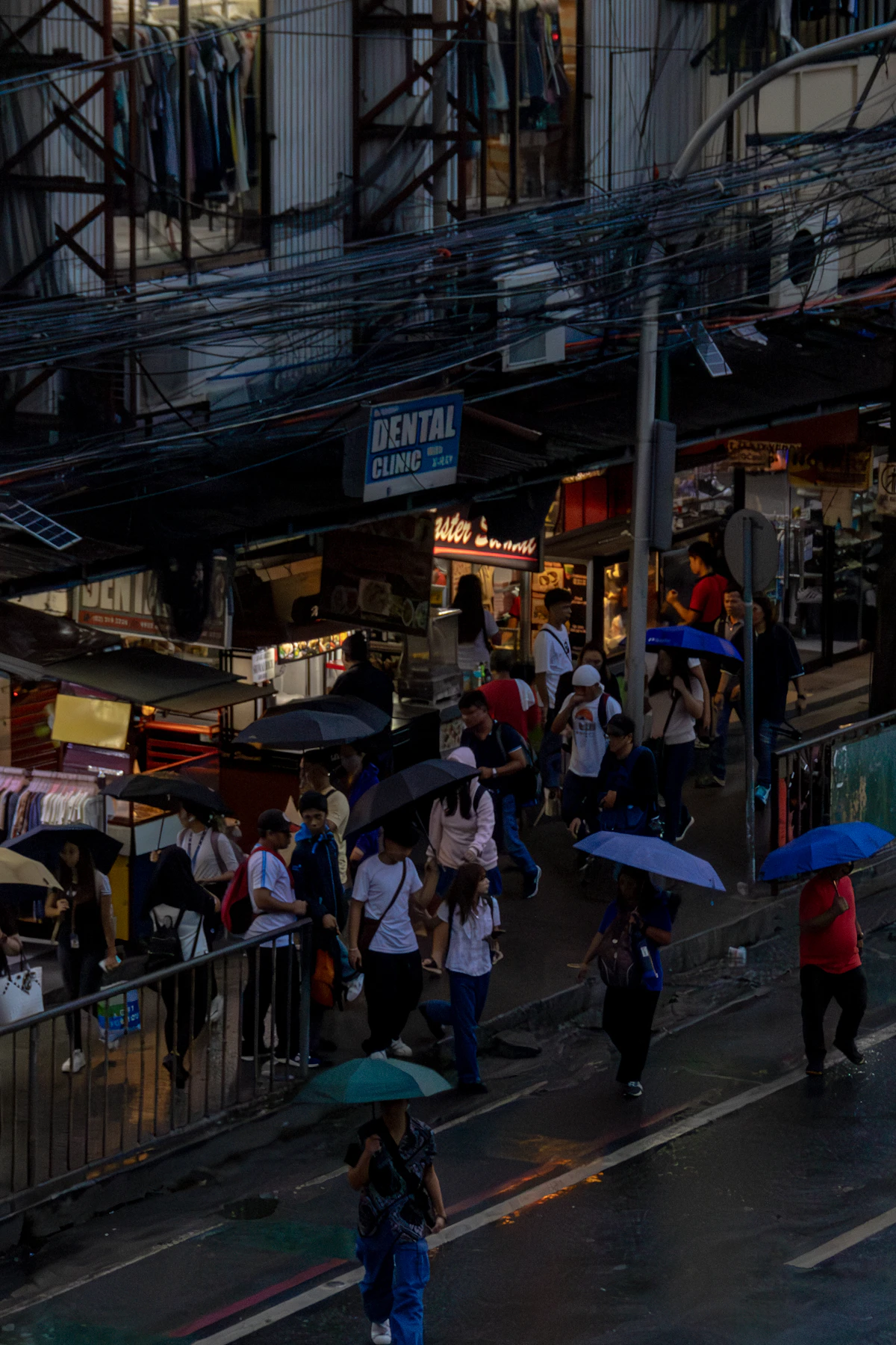 Pedestrians holding umbrellas while walking on a wet Manila street during the rainy season