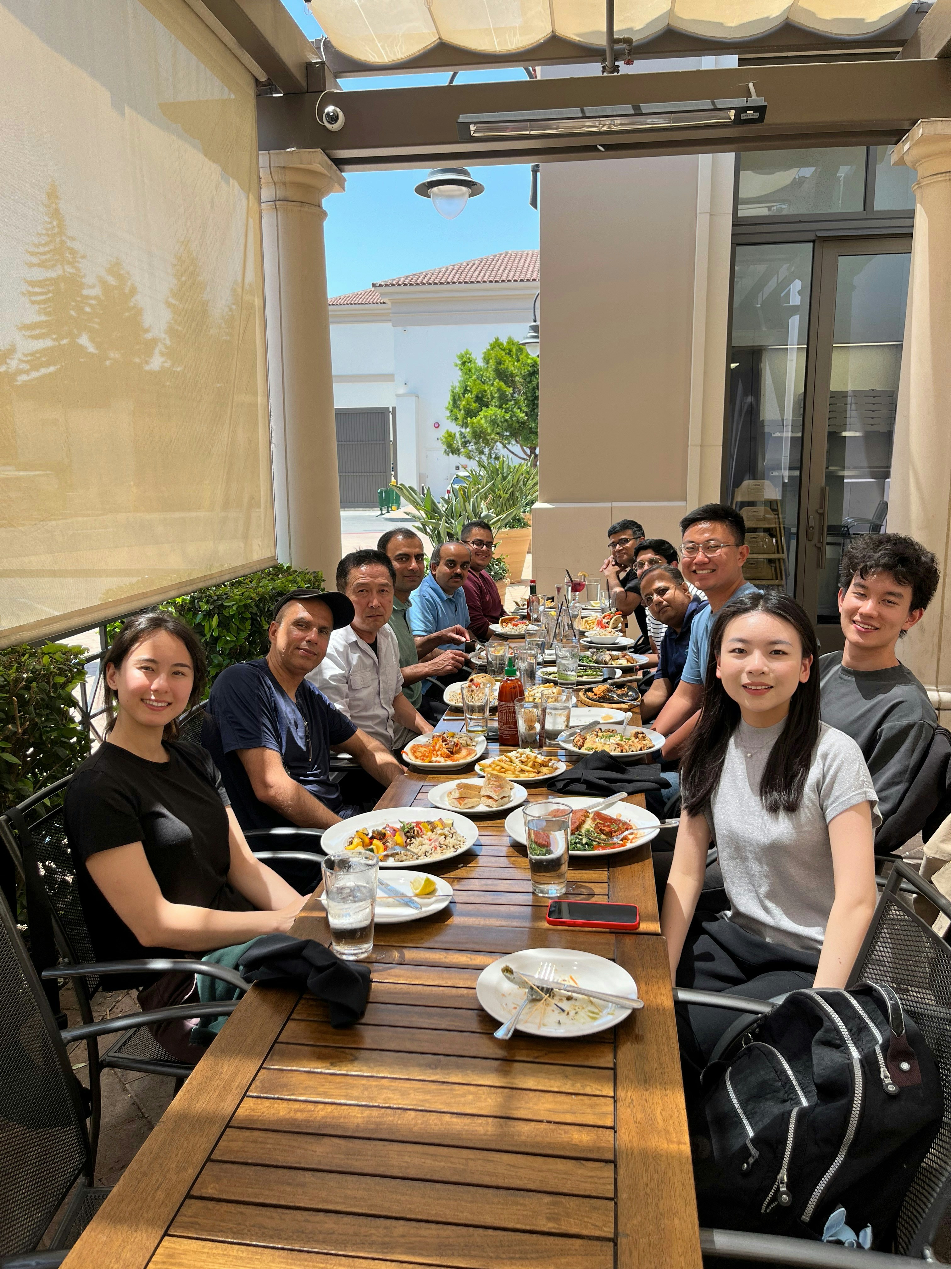 Diverse group of people sharing a meal outdoors in warm afternoon sunlight, laughing and connecting