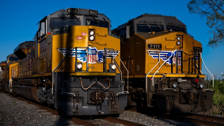 A yellow train traveling down train tracks next to a forest