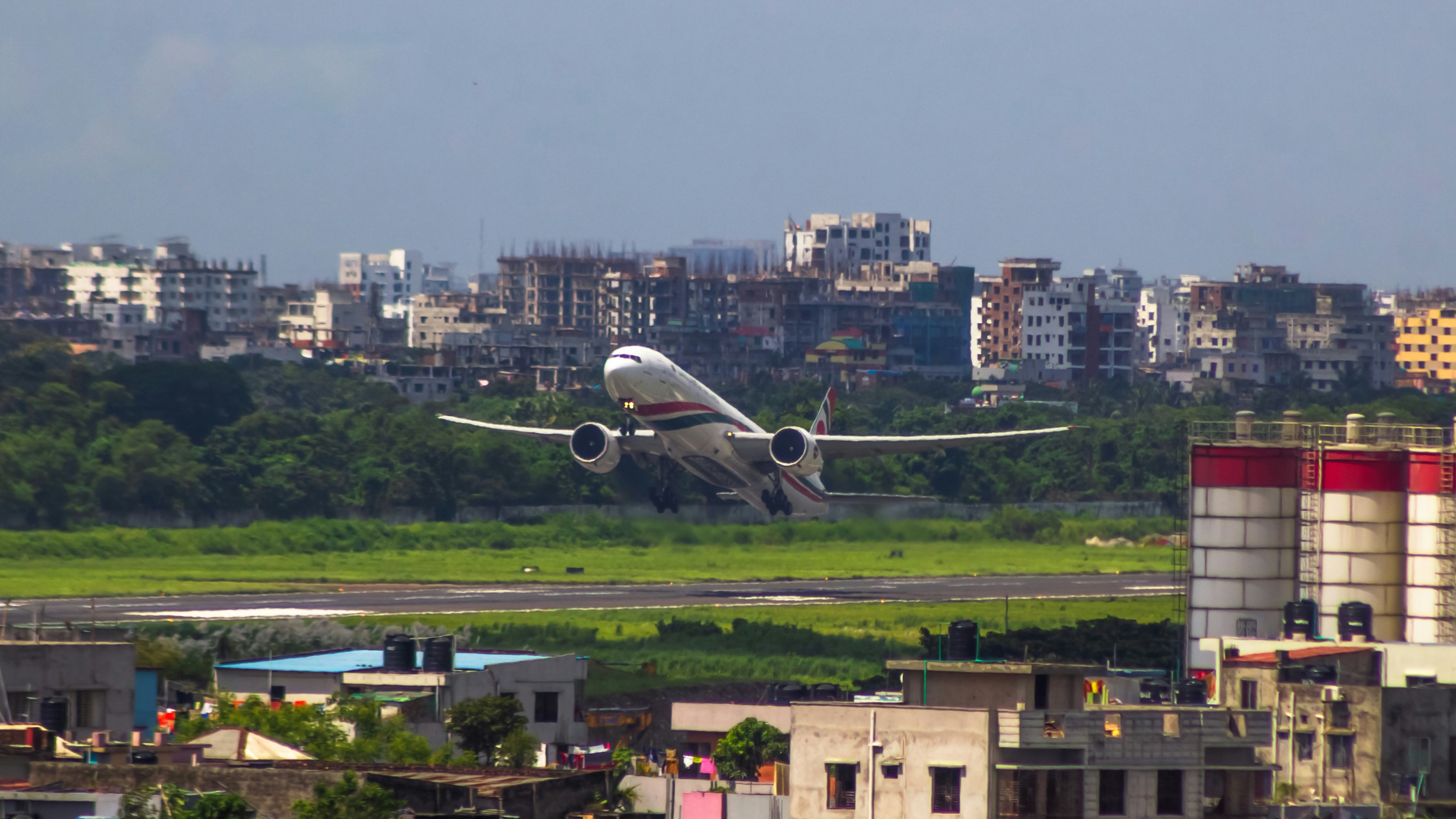 An airplane taking off from a runway in a city, Biman Bangladesh Airlines | Boeing 777-300ER (S2-AHM). Flying from DAC -> KUL