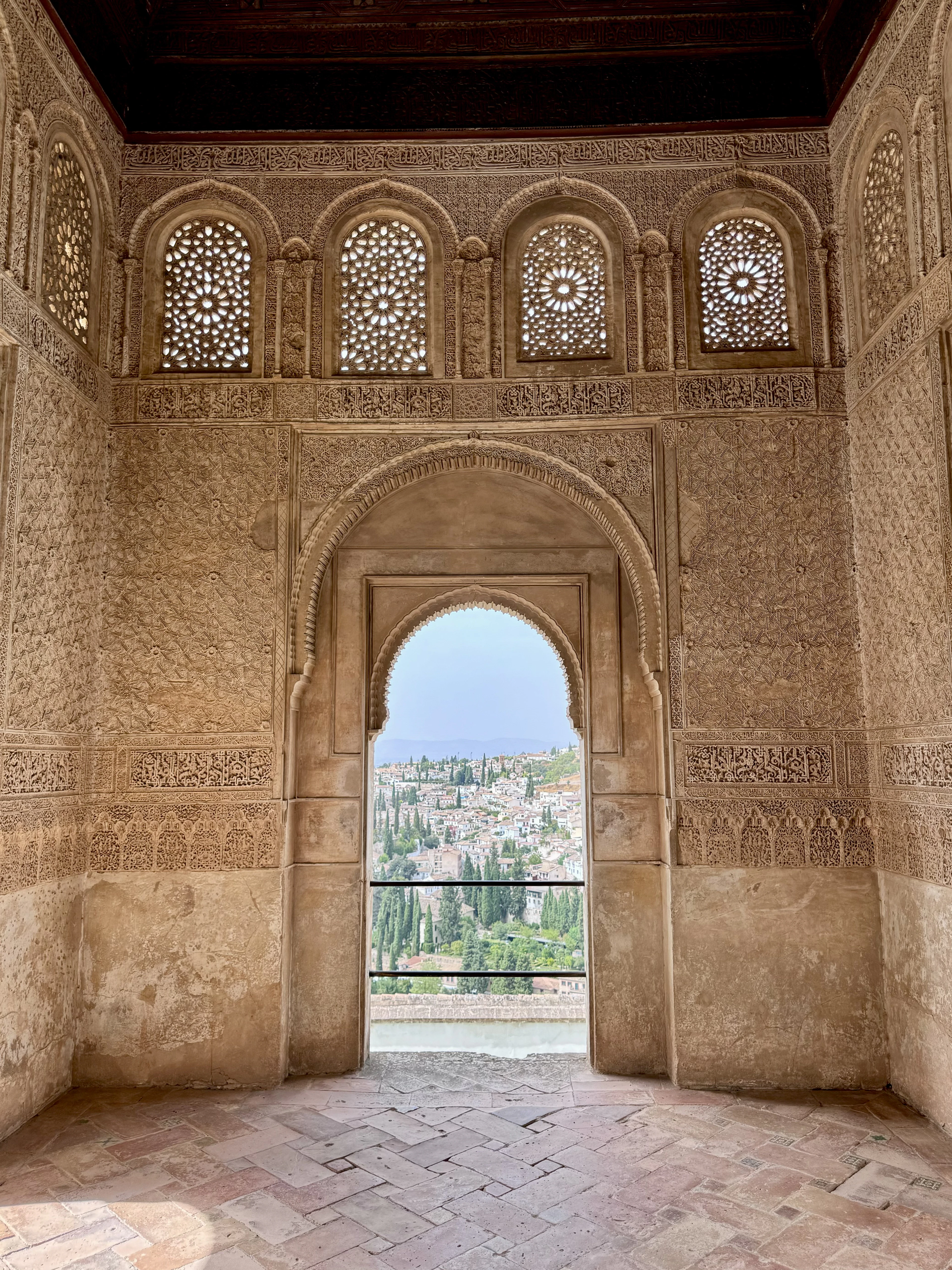 An ornately carved Moorish archway and latticed windows frame a view over Granada's Albaicín hillside.