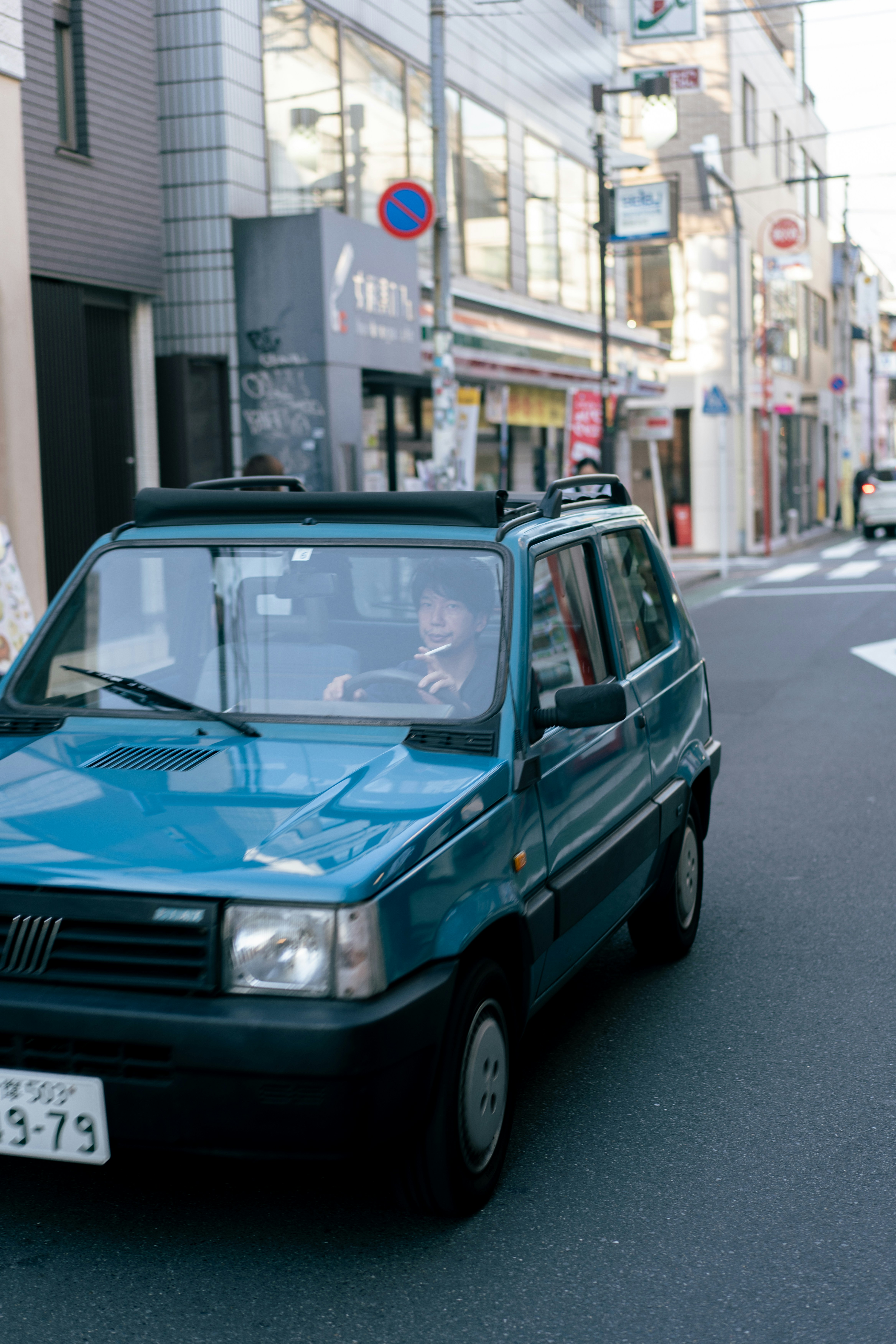 A blue car driving down a street next to tall buildings