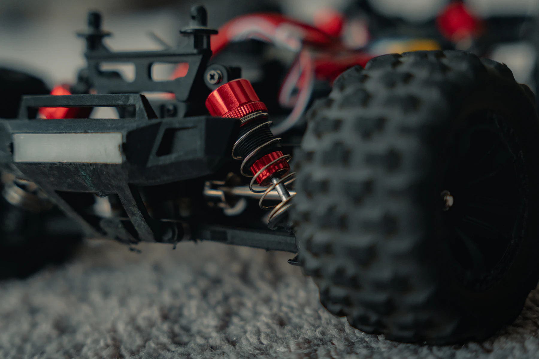 Close-up of a red coil-over shock and a knobby front tire on a truck parked on carpet
