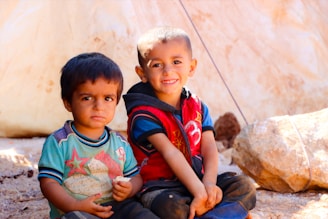 Two young boys sitting next to each other on the ground