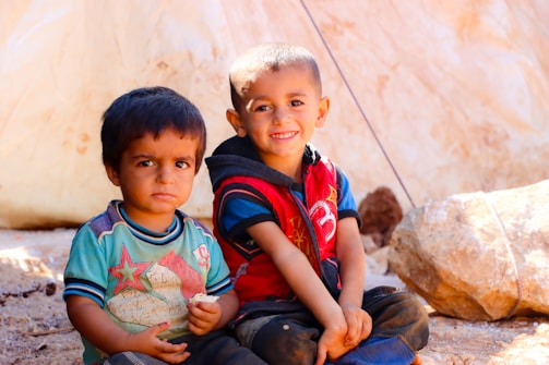 Two young boys sitting next to each other on the ground
