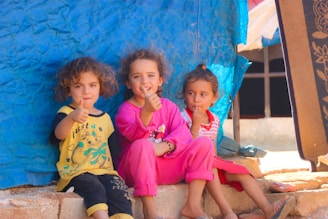 Three little girls sitting on a ledge in front of a blue tarp