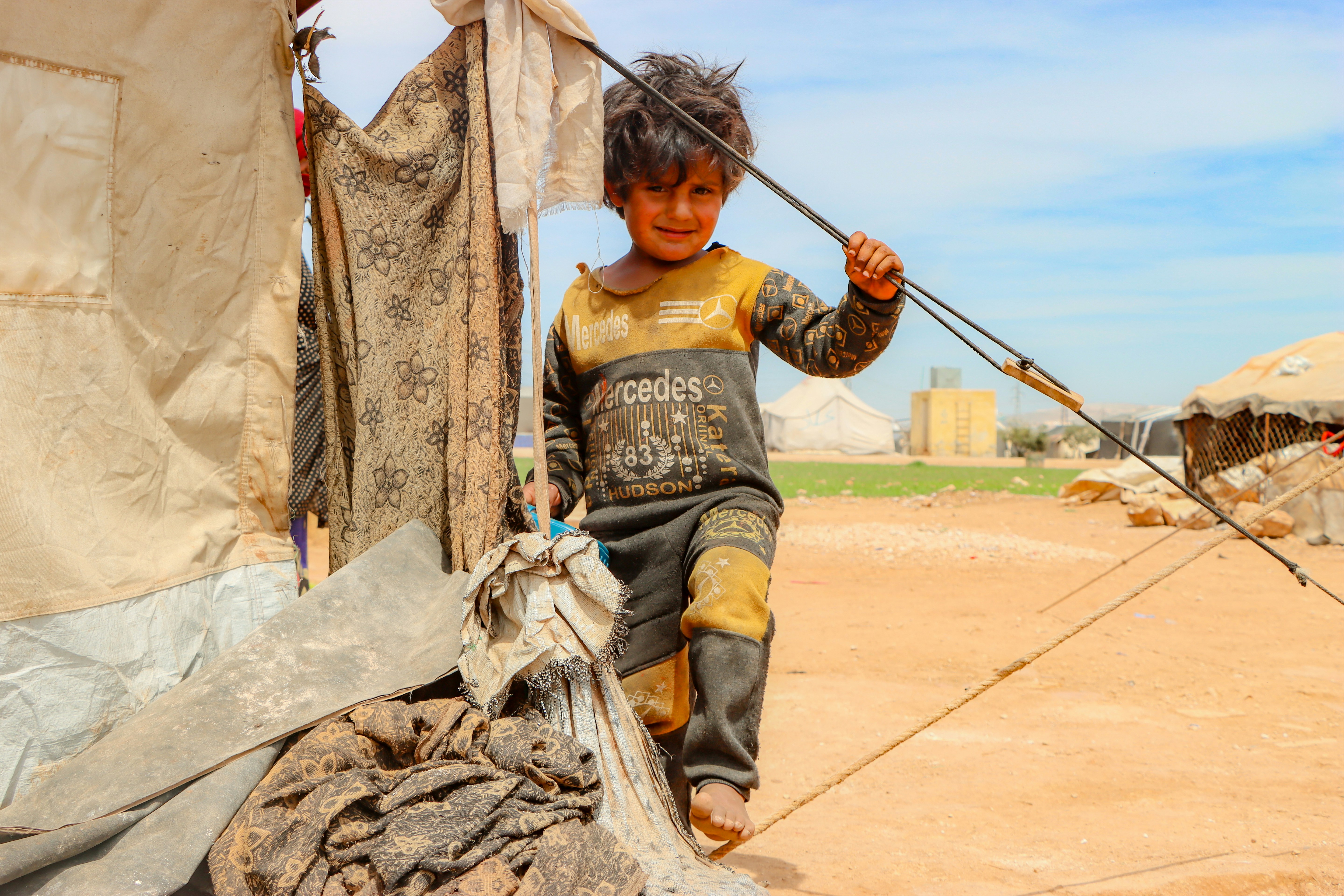 A young boy holding a stick in front of a tent