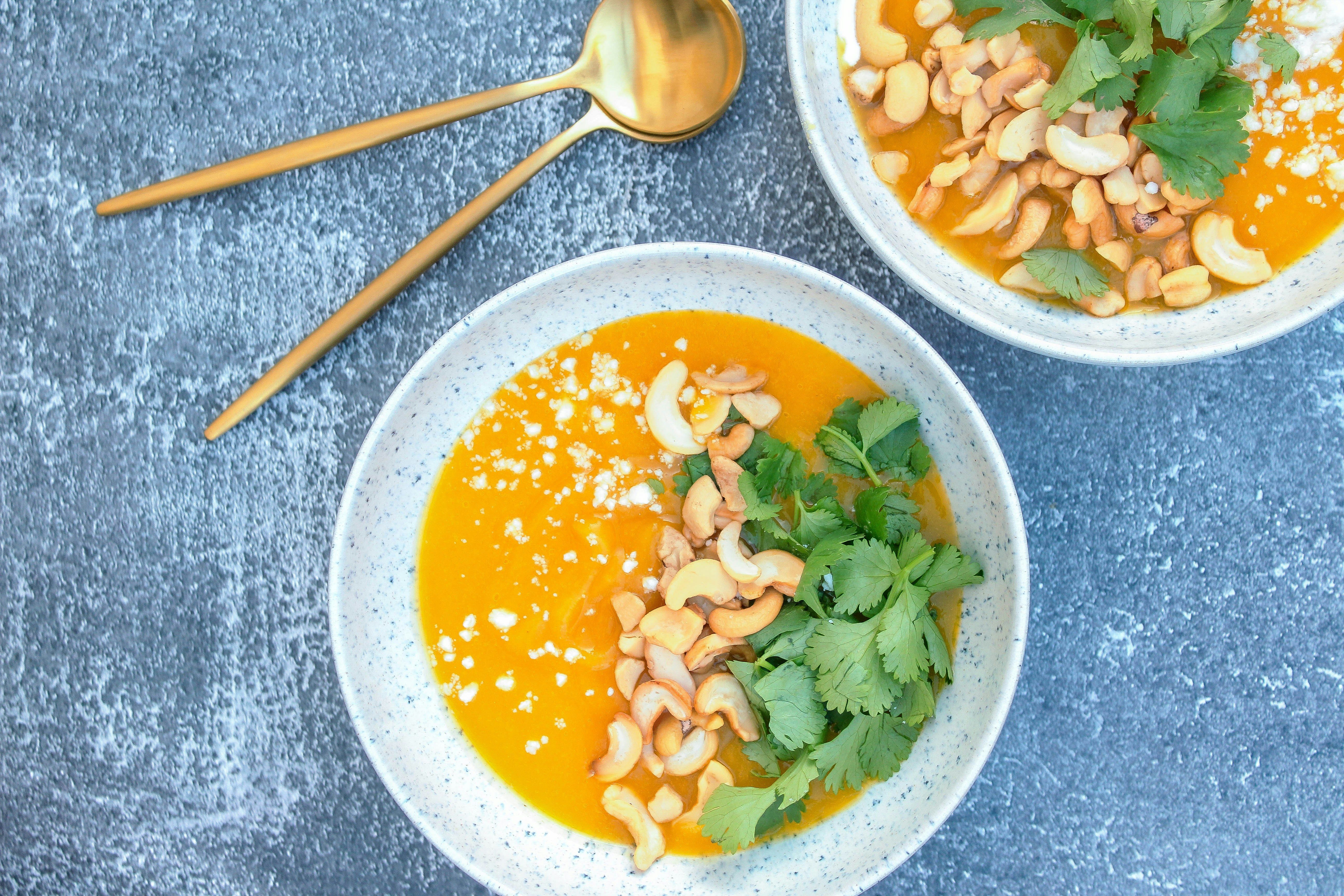 Two bowls of carrot soup on a blue surface