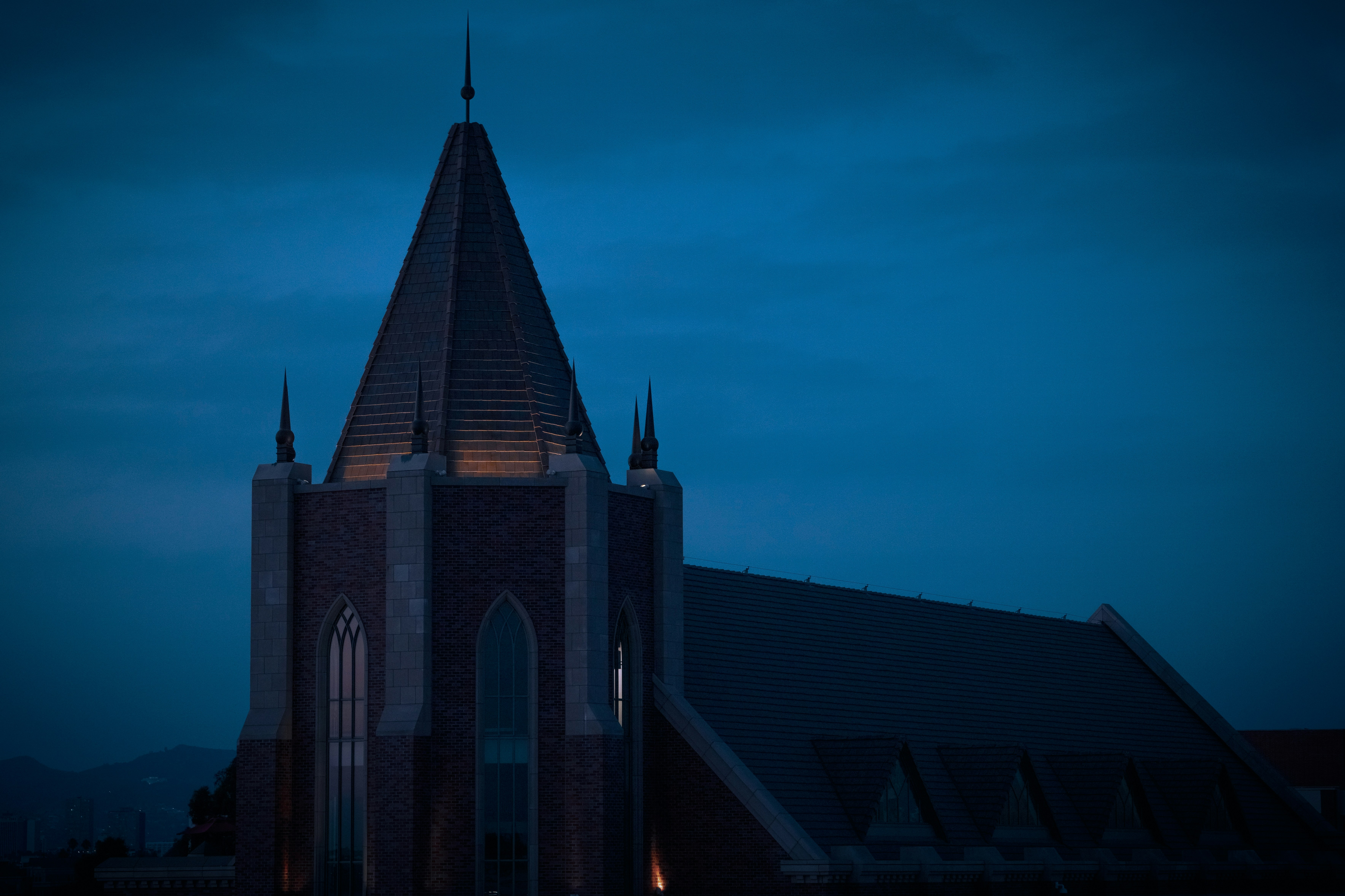 A striking gothic church rises against a deep blue twilight sky in Los Angeles. The illuminated spire and pointed arches