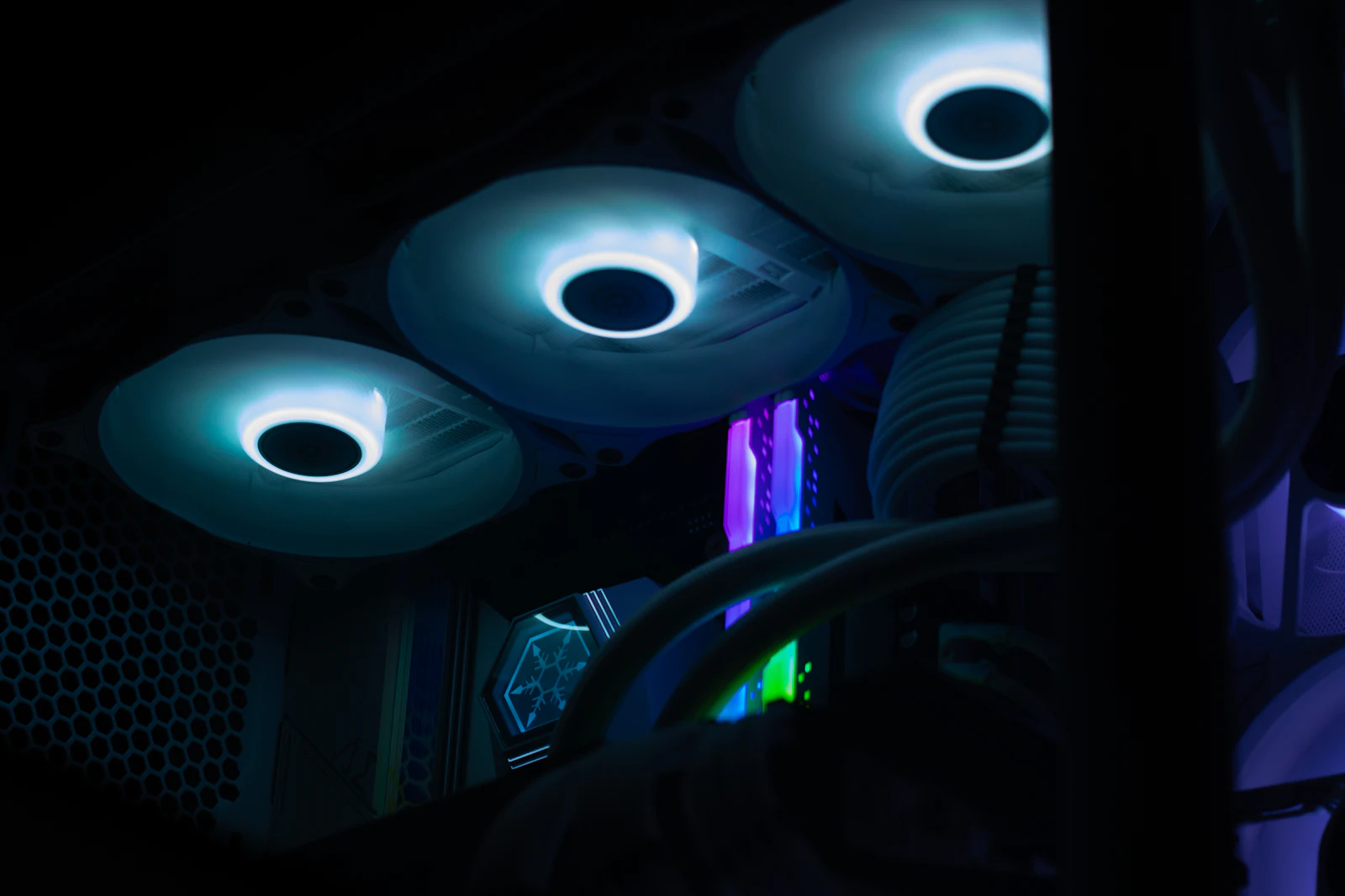 Intérieur d&rsquo;un PC gamer dans le noir avec ventilateurs lumineux cyan, barrettes de RAM RGB et watercooling