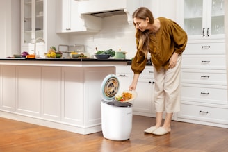 A woman standing next to a trash can in a kitchen