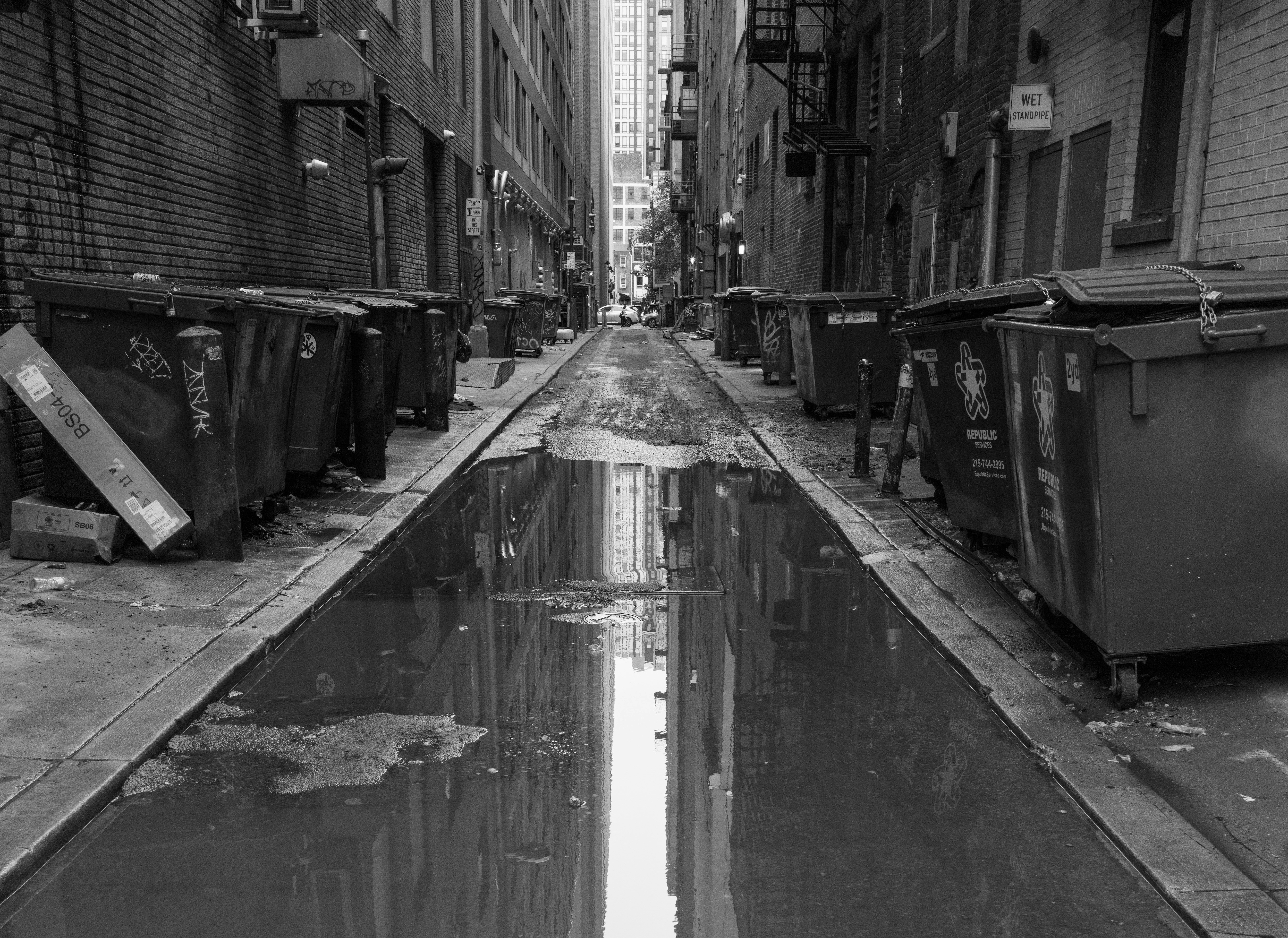 A narrow city street with trash cans on the side of it