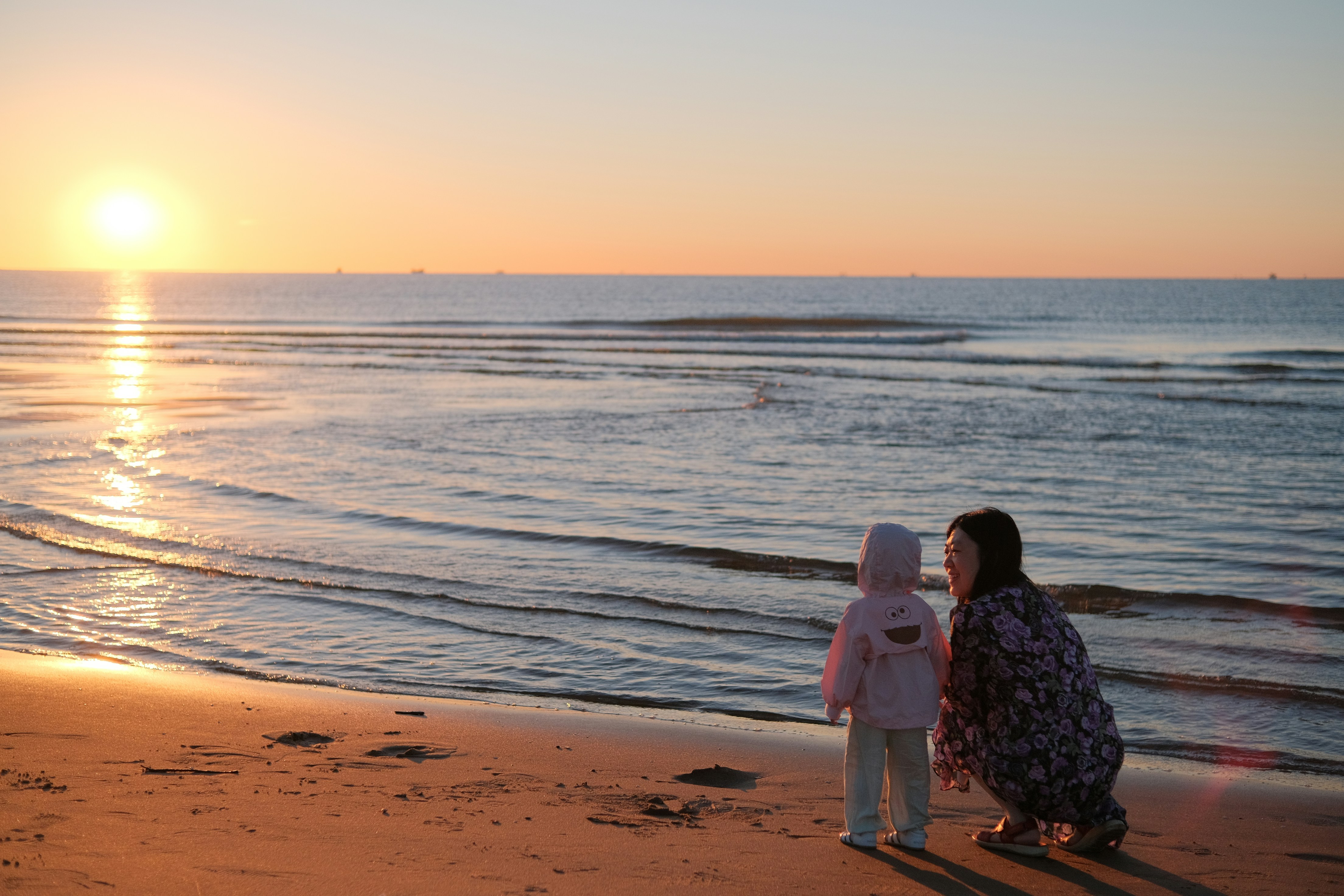 Seorang wanita dan seorang anak berdiri di pantai saat matahari terbenam