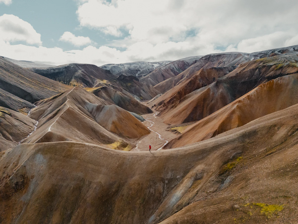 A gravel track winding up a valley between bare, striped mountains at Landmannalaugar under white cloud