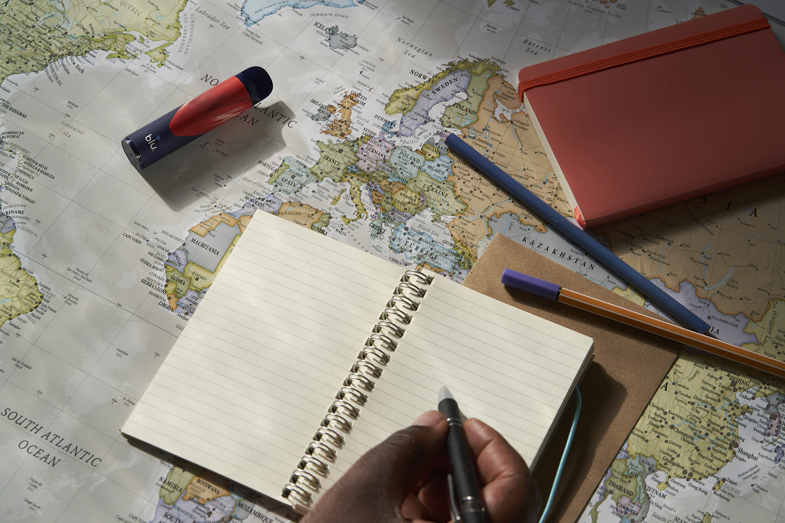 A hand writes notes in a notebook over a world map.
